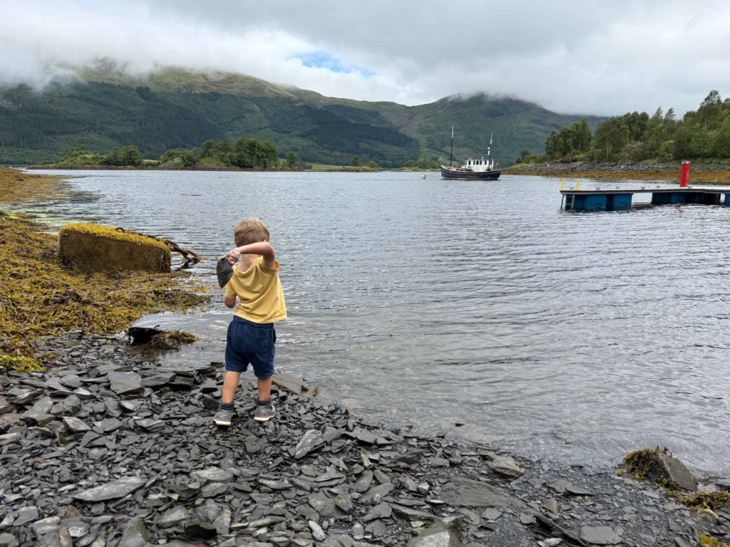 Toddler throwing rocks into the lake outside The Isles of Glencoe Hotel