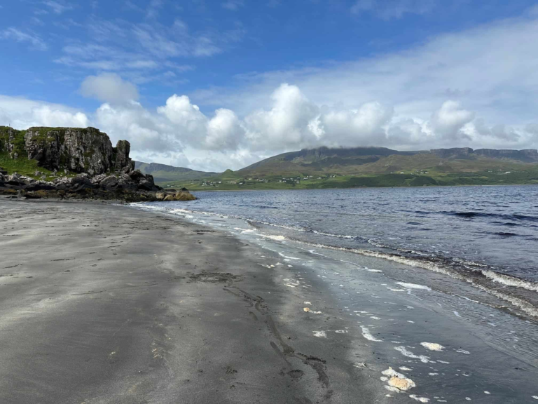 Staffin Beach on the Isle of Skye - an open beach with black sand with dramatic hills landscape.