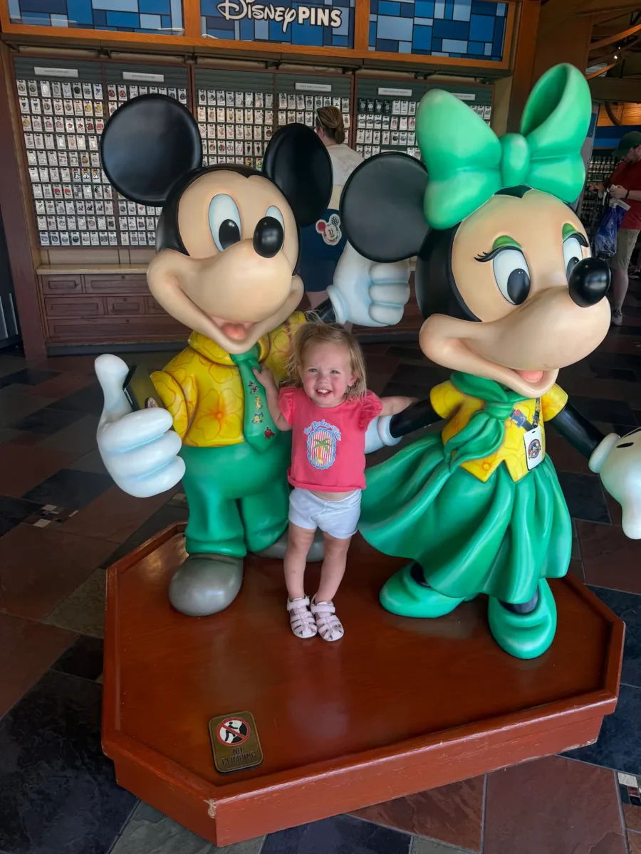 Toddler girl poses between mickey and minnie mouse at disney springs